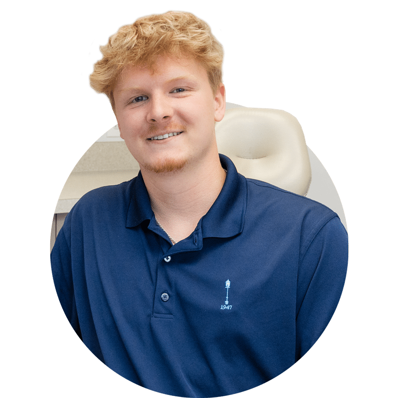 A person is seated indoors, wearing a navy-blue polo shirt. The background features neutral-colored walls and cabinets, suggesting an office setting.