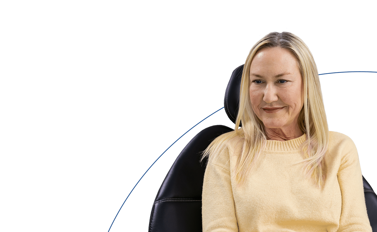 A person in a yellow sweater sits on a chair, looking relaxed with a solid blue and white background.