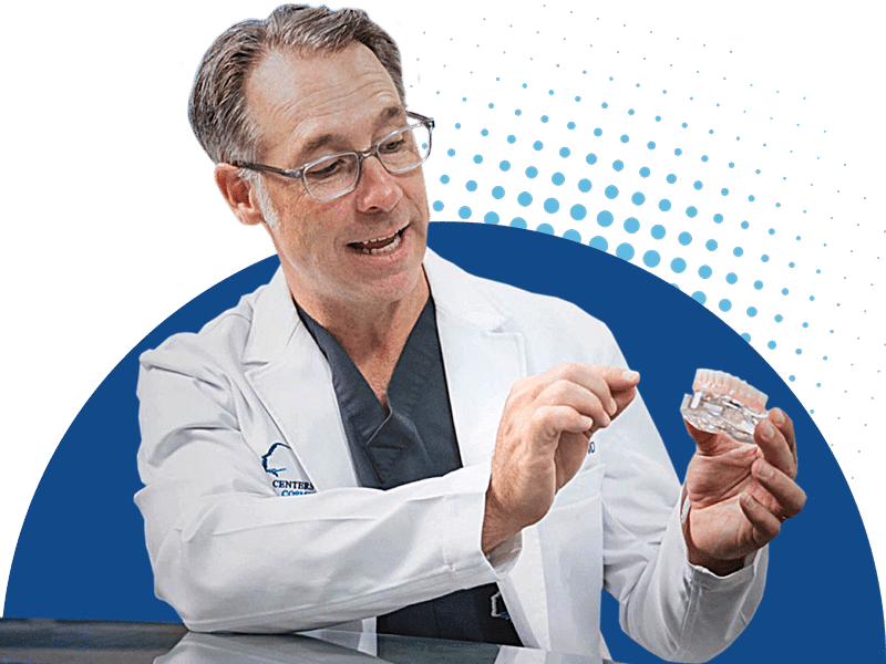 A person in a white coat demonstrates a dental model against a blue, dotted background, illustrating dental care or education.