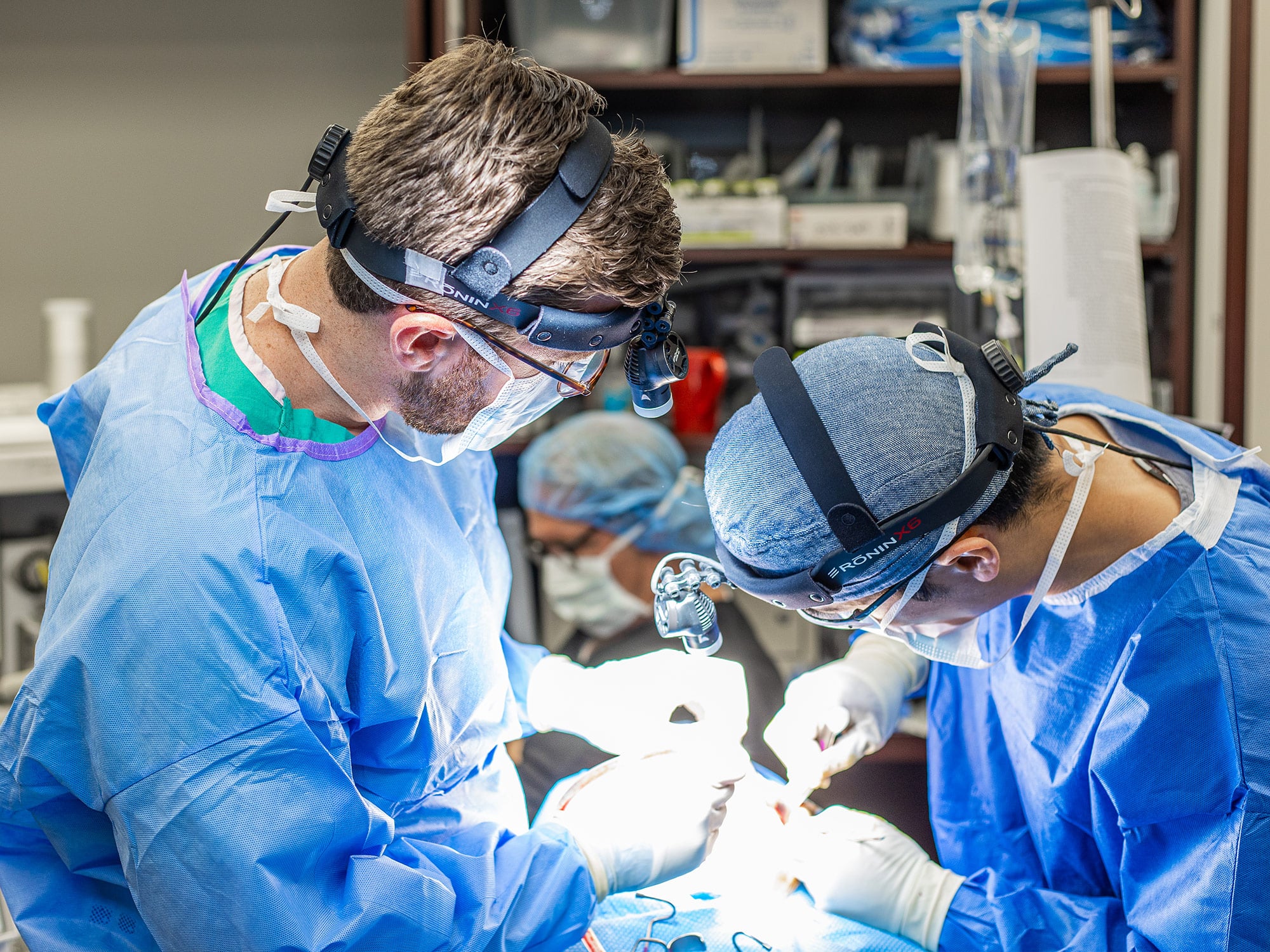 Two persons in surgical attire perform a medical procedure with precision, surrounded by medical equipment in a healthcare setting.