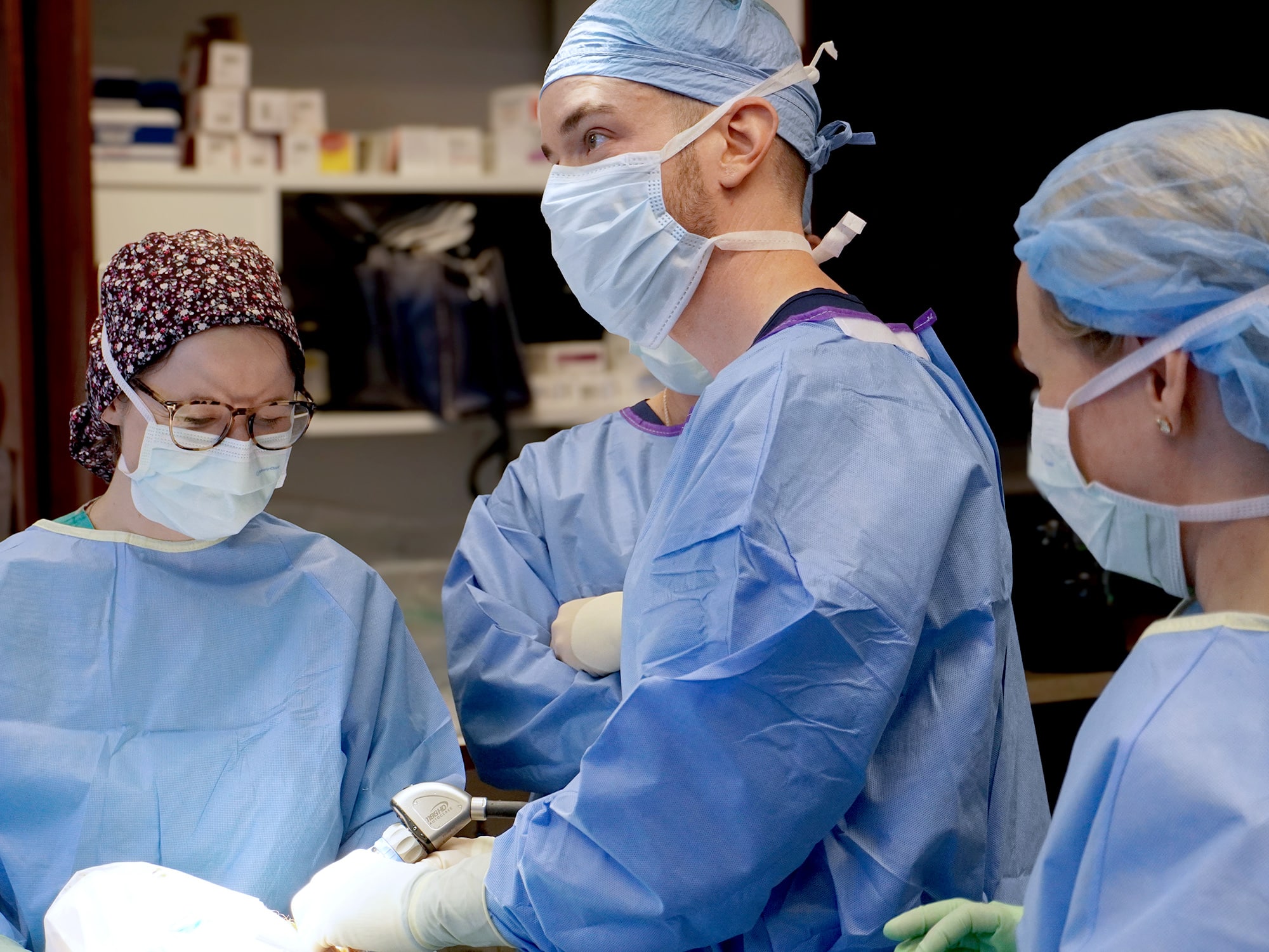 Four people wearing surgical masks and gowns collaborate in an operating room, focusing intently on a medical procedure.