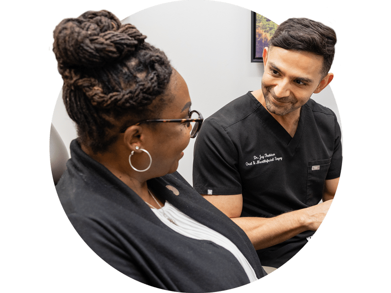 Two people are sitting in an office. One is wearing scrubs, and they are engaged in a conversation, smiling at each other.