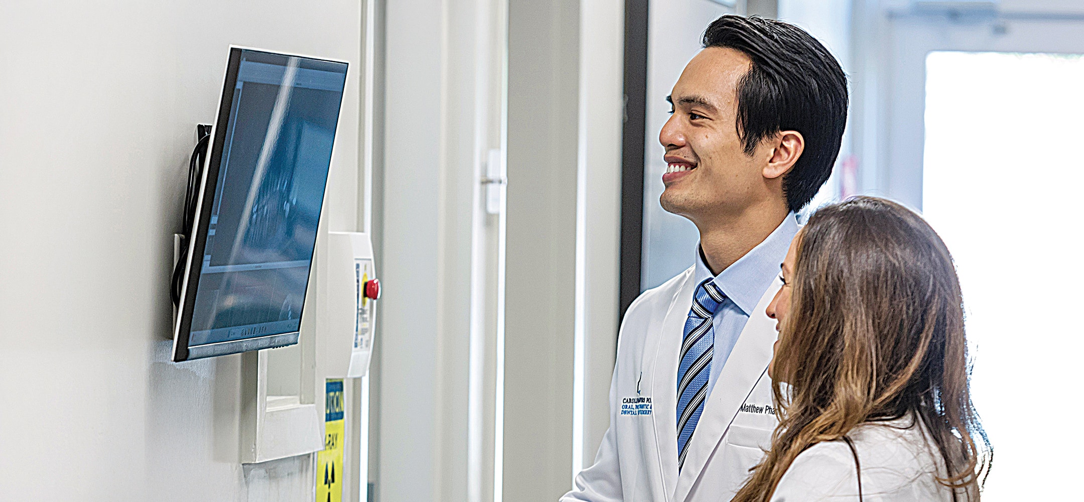 Two people in medical attire smile while viewing X-ray images on a screen in a clinical setting.
