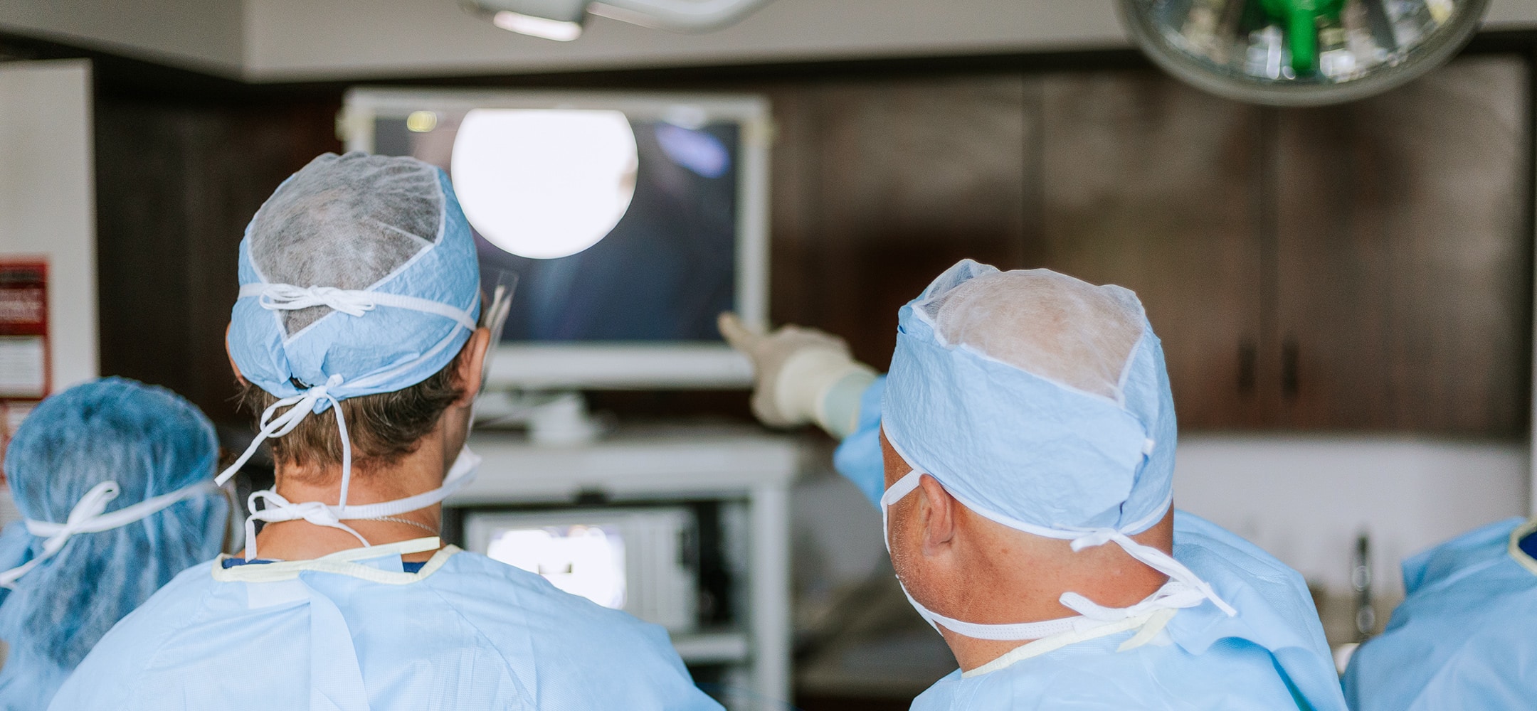 Persons in surgical attire focus on a monitor in an operating room, collaborating and analyzing medical imagery during a procedure.