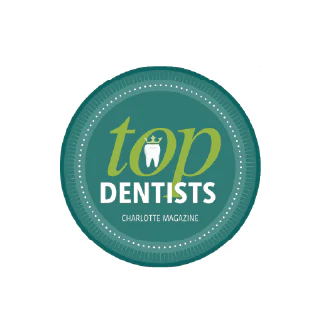 A circular emblem features "Top Dentists" with a tooth icon, awarded by Charlotte Magazine, set against a teal background with a dotted border.