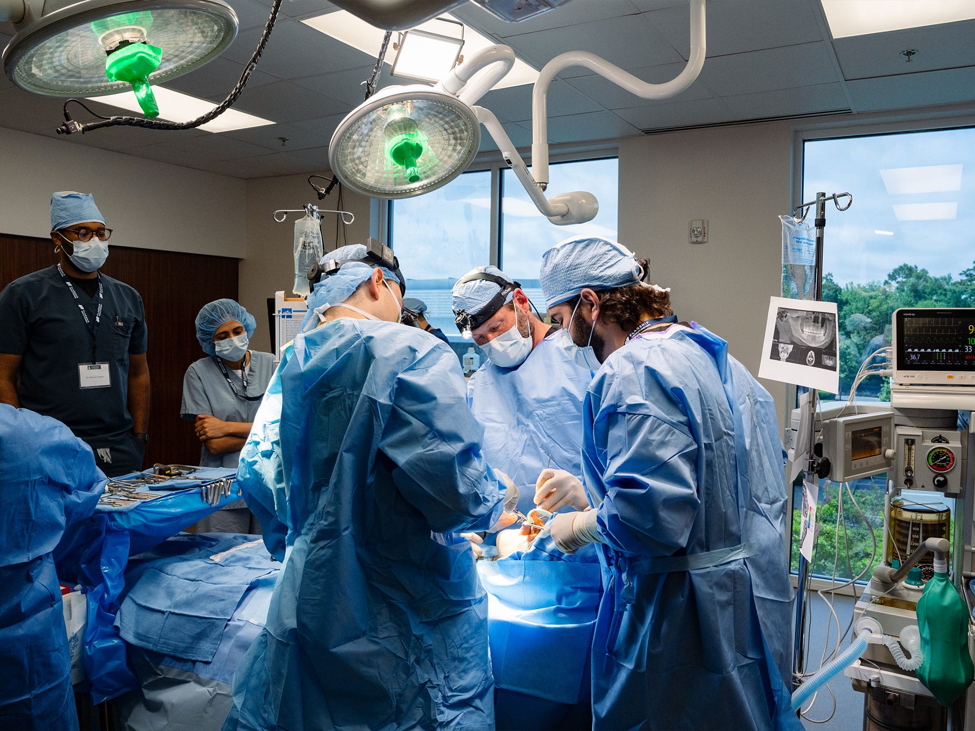 Medical team in blue scrubs performs surgery in a well-lit operating room, with advanced equipment and people attentively monitoring the procedure.