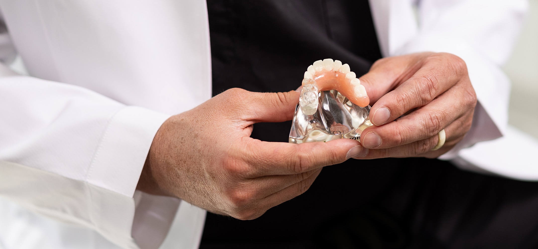 A person in a white coat holds a dental model with teeth, demonstrating oral healthcare or dental practice, emphasizing tooth structure.