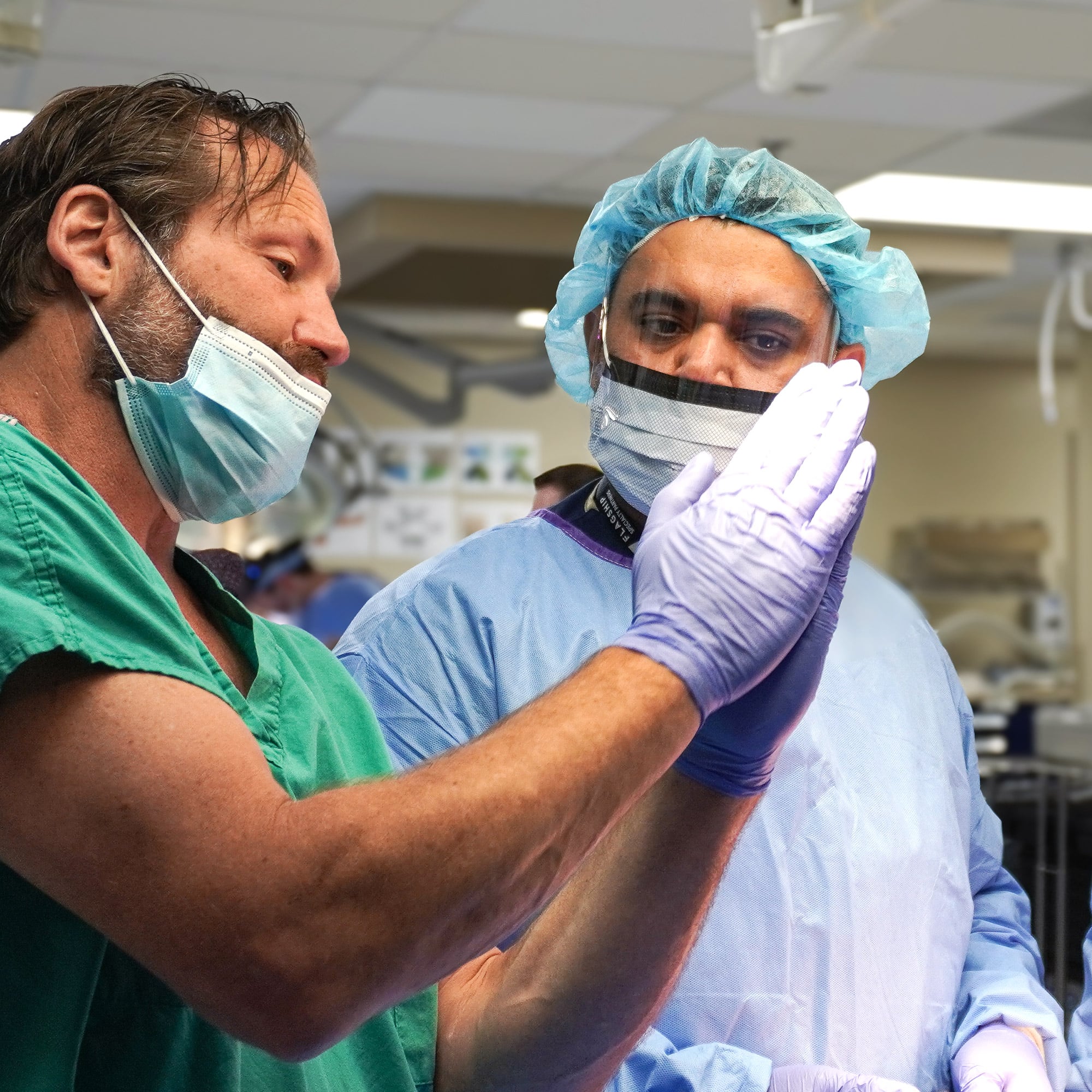 Two medical professionals in scrubs and masks are intently discussing something in a hospital setting, with one gesturing towards the other.