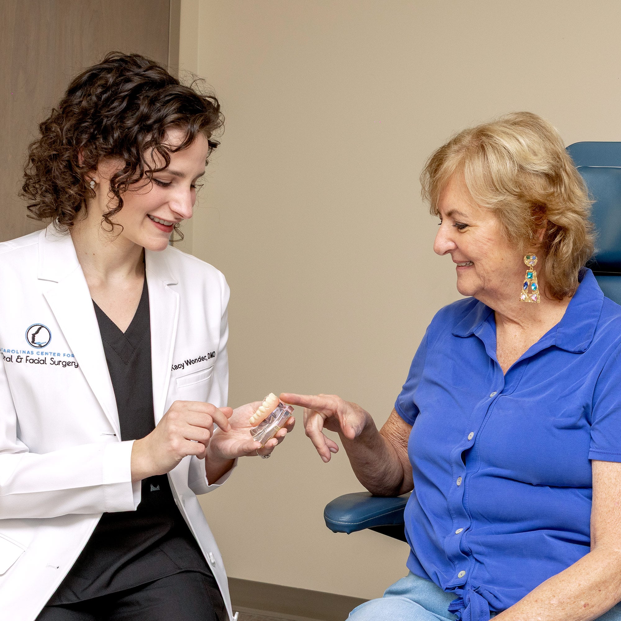Two people in a dental office, one showing teeth model to the other with a friendly interaction.