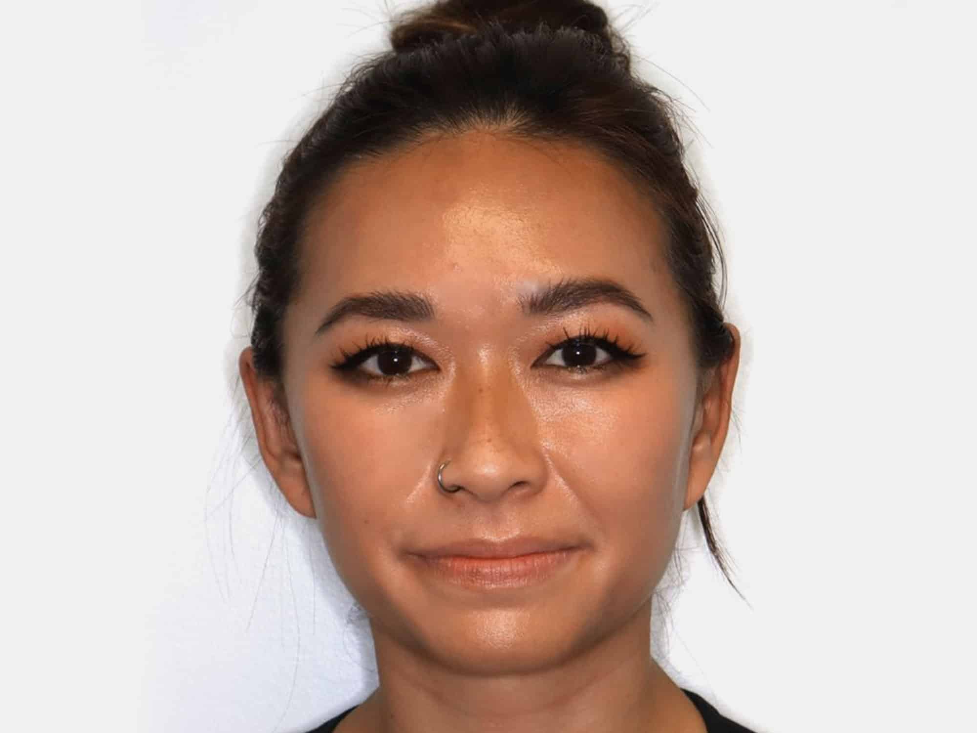 A person with a bun hairstyle and a nose ring, set against a plain white background, looking directly at the camera.